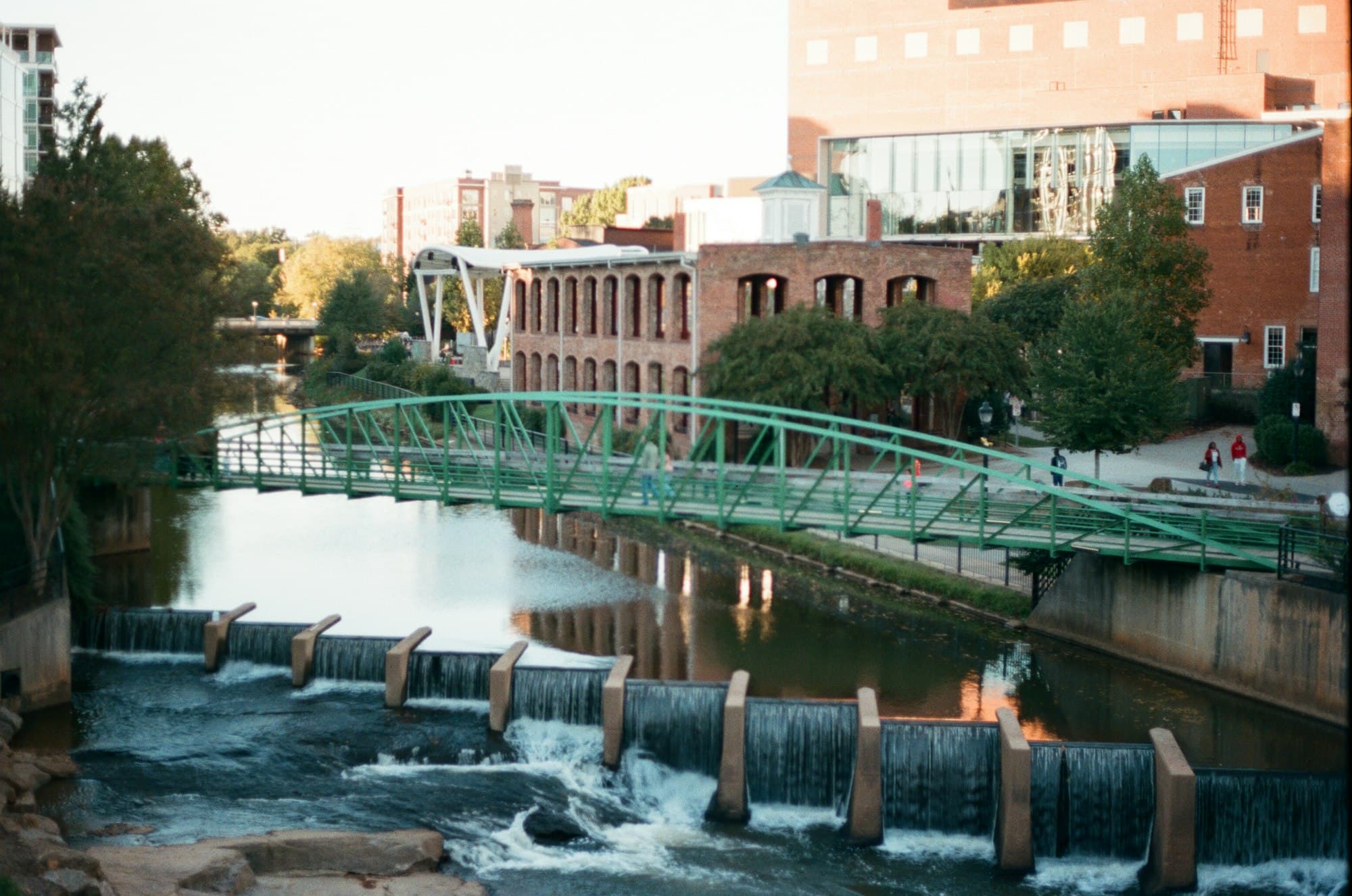 The green Liberty Bridge arching over the Reedy River falls at Falls Park in downtown Greenville.