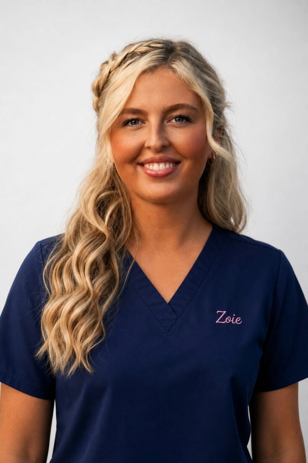 Zoie Poole, smiling, in navy scrubs embroidered with her name.