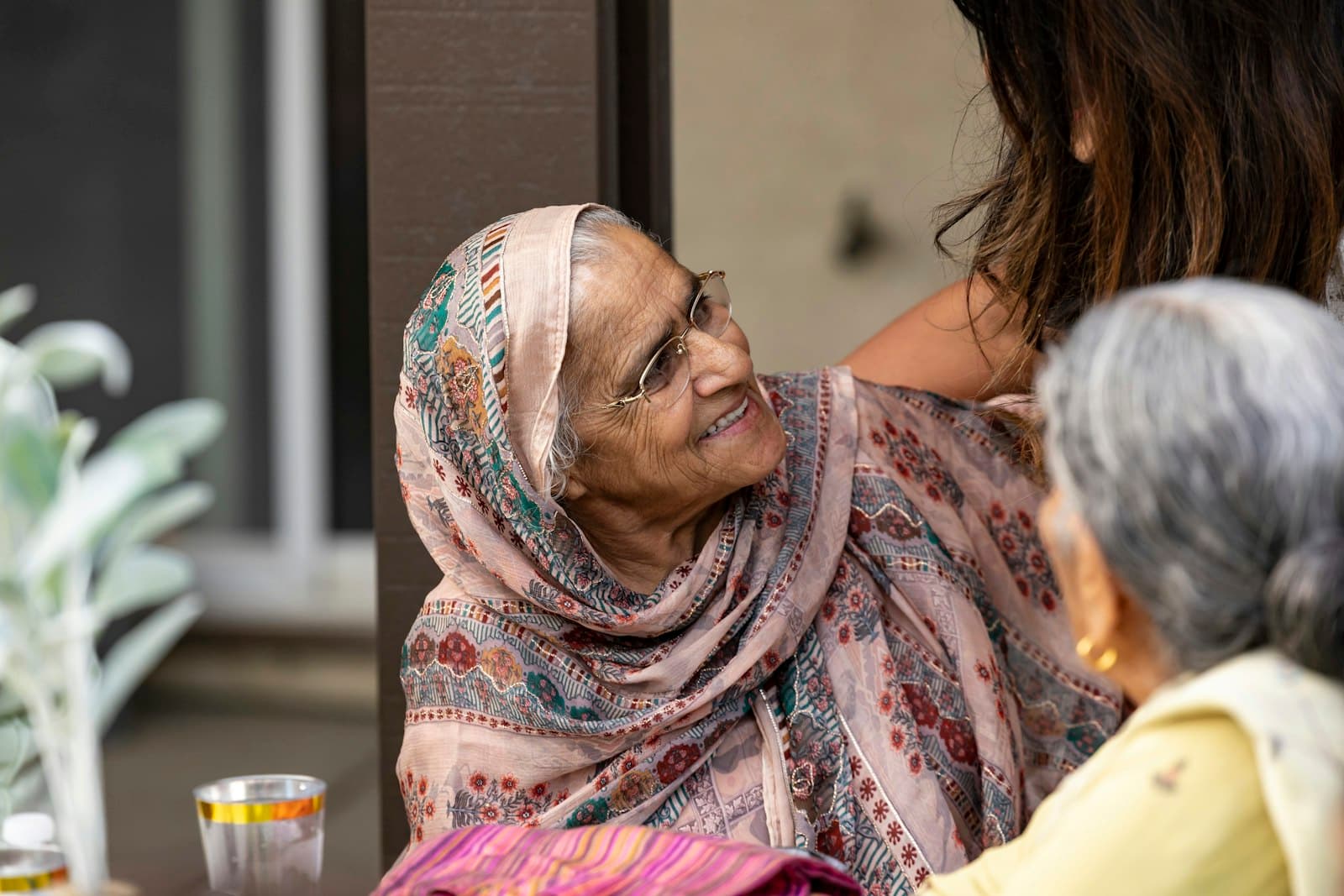 A grandmother in a patterned shawl smiles up at her family on the porch.